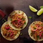 Three cochinita pibil tacos and lime wedges